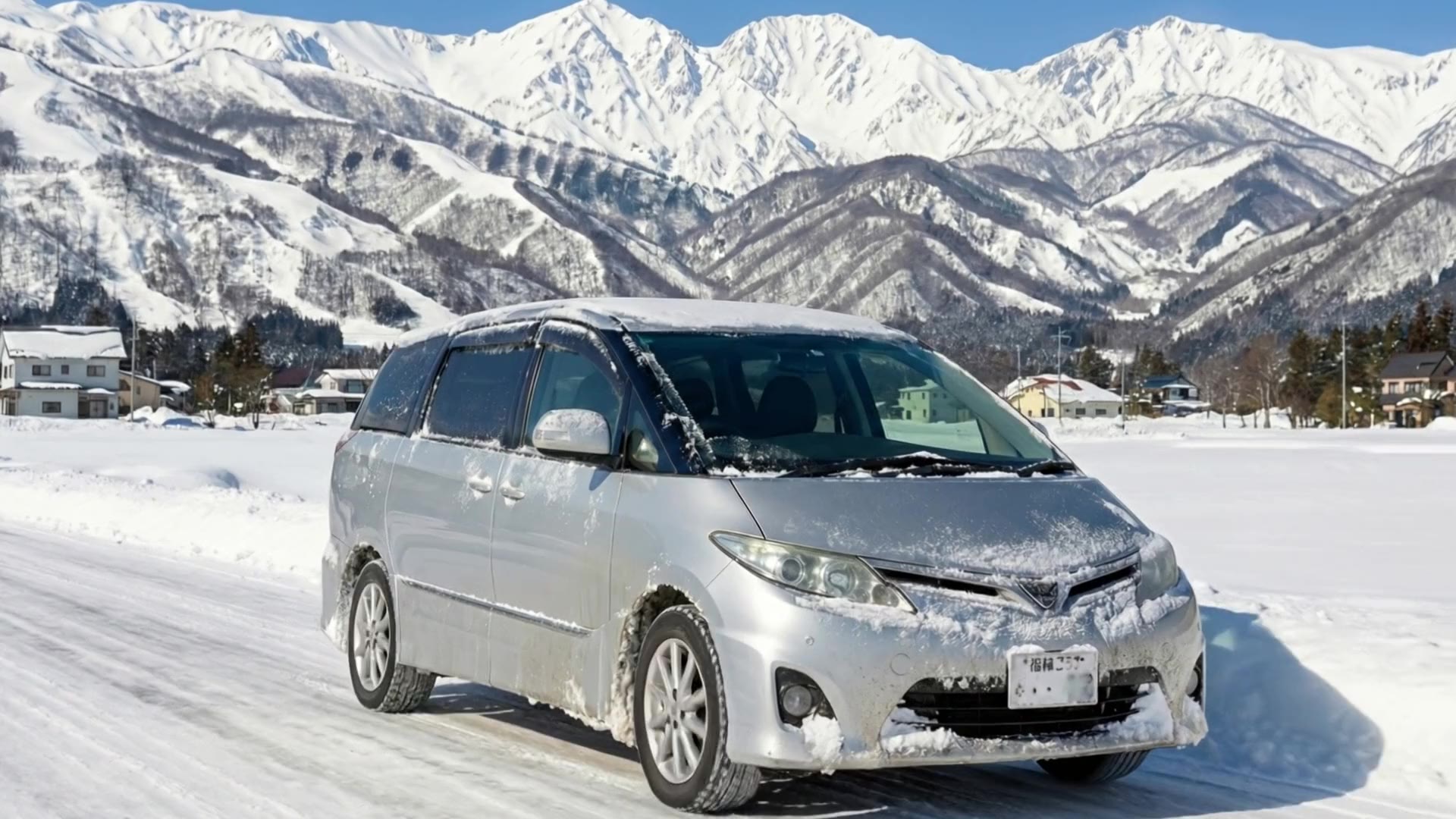 北アルプスを背景に白馬の雪道を走るレンタカー
