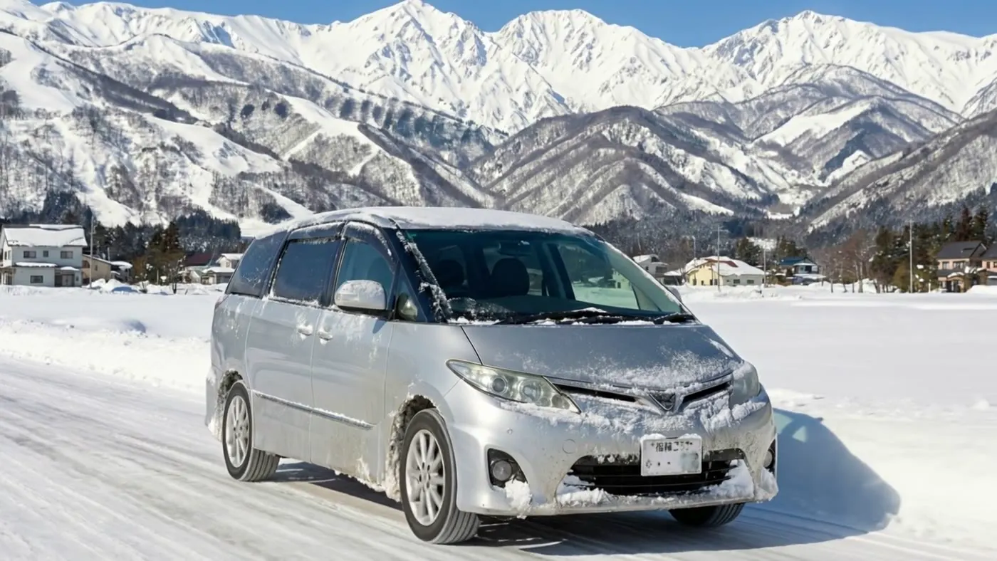 北アルプスを背に雪道を走る白馬レンタカーのミニバン（4WD）